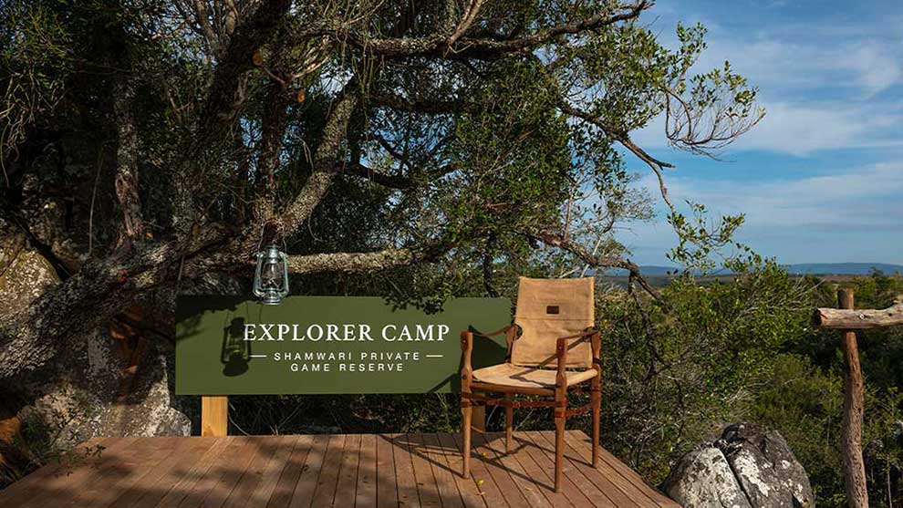 02 Shamwari A camping chair next to a—big south african tree and sign that reads explorer camp 1